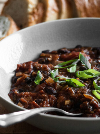 Photo of a bowl with a spoon in it. In the bowl are black beans with sliced green onions on top. A loaf of sliced bread rests in the background. Photo by Frank Holleman on Unsplash.