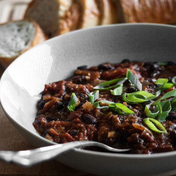 Photo of a bowl with a spoon in it. In the bowl are black beans with sliced green onions on top. A loaf of sliced bread rests in the background. Photo by Frank Holleman on Unsplash.