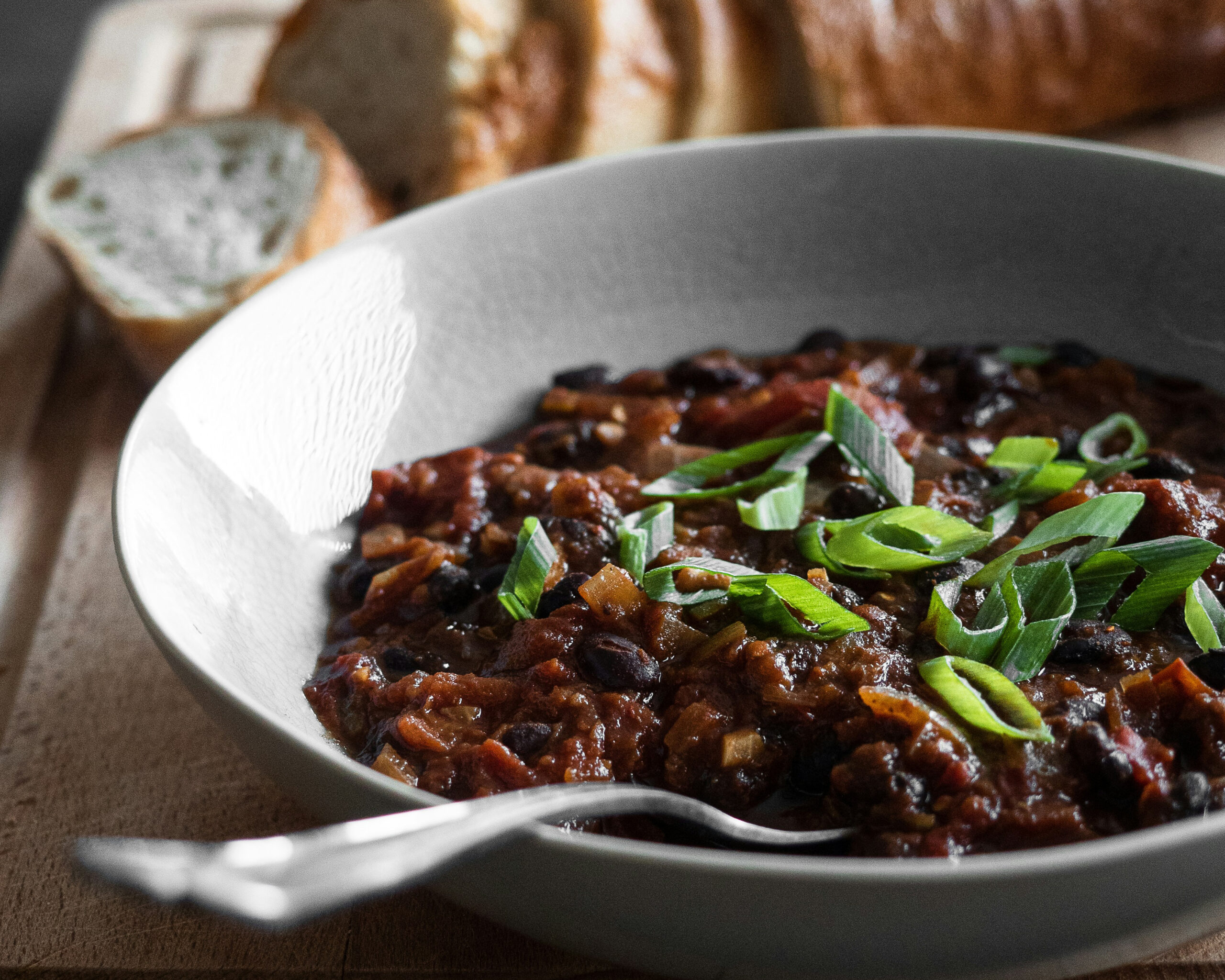 Photo of a bowl with a spoon in it. In the bowl are black beans with sliced green onions on top. A loaf of sliced bread rests in the background. Photo by Frank Holleman on Unsplash.