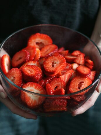 Two hands holding a glass bowl full of sliced strawberries. Photo by Shane on Unsplash