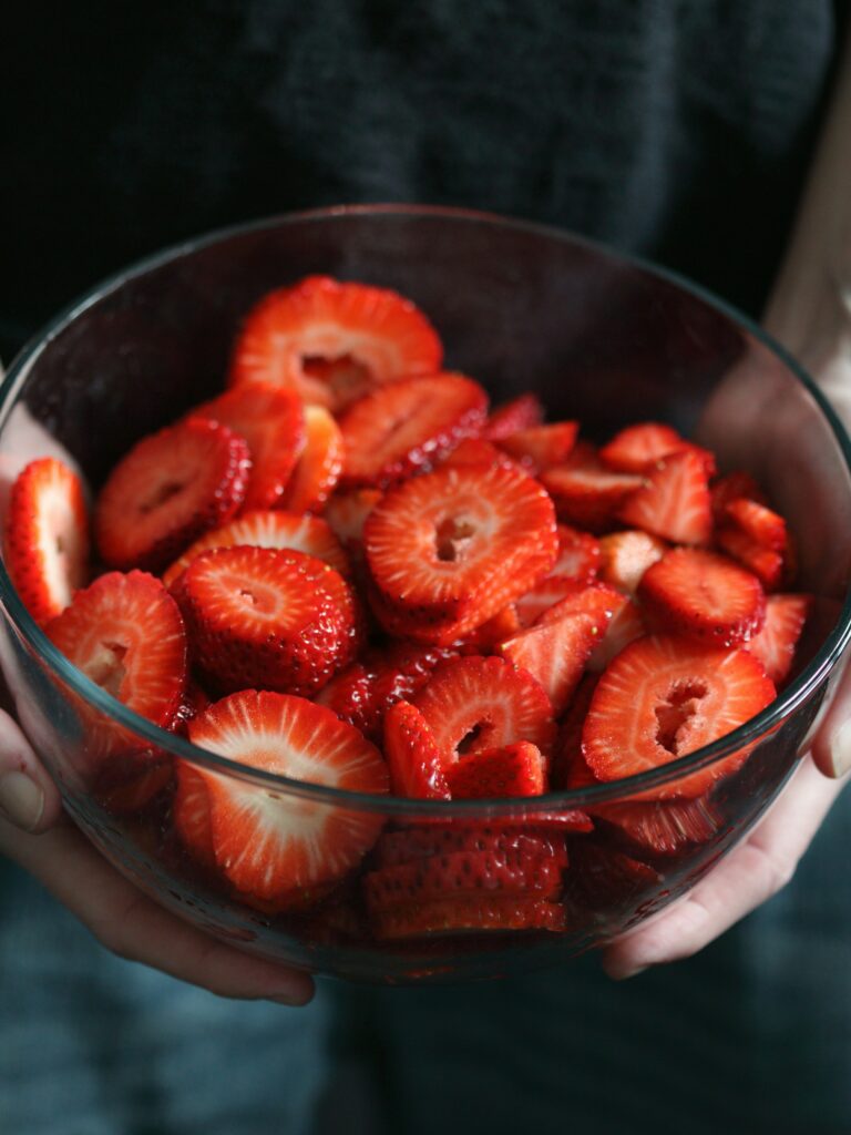 Two hands holding a glass bowl full of sliced strawberries. Photo by Shane on Unsplash