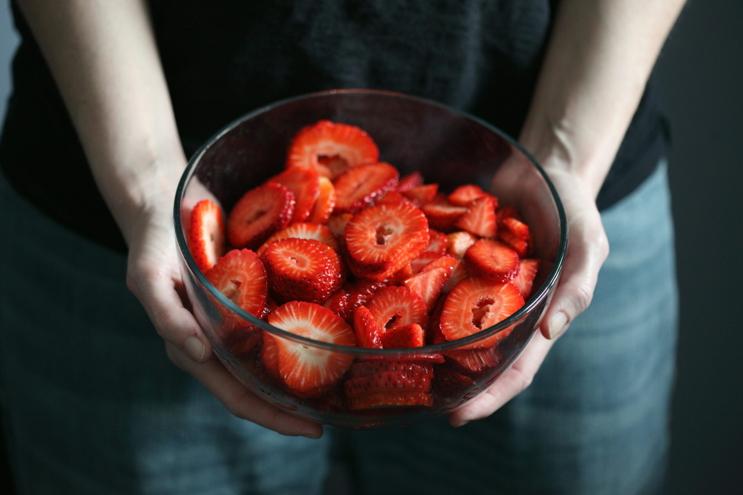 Two hands holding a glass bowl full of sliced strawberries. Photo by Shane on Unsplash