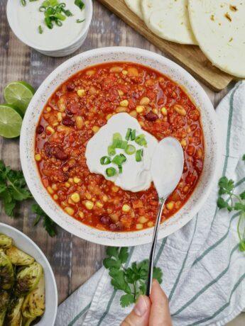 White bowl on a tablecloth. In the bowl is vegetable chili with s dollop of sour cream in the center, chives sprinkled on top. A spoon coated in sour cream rests in the bowl. Photo by stephanie monfette on Unsplash