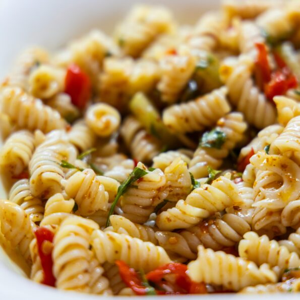 A white bowl contains spiral pasta, diced vegetables, and a vinaigrette dressing. Photo by engin akyurt on Unsplash.