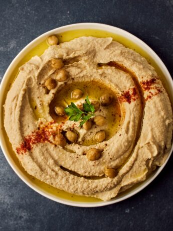 White bowl on a dark table. Inside the bowl is hummus garnished with chickpeas and herbs. Photo by Ludovic Avice on Unsplash