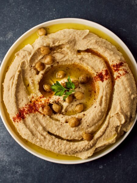 White bowl on a dark table. Inside the bowl is hummus garnished with chickpeas and herbs. Photo by Ludovic Avice on Unsplash