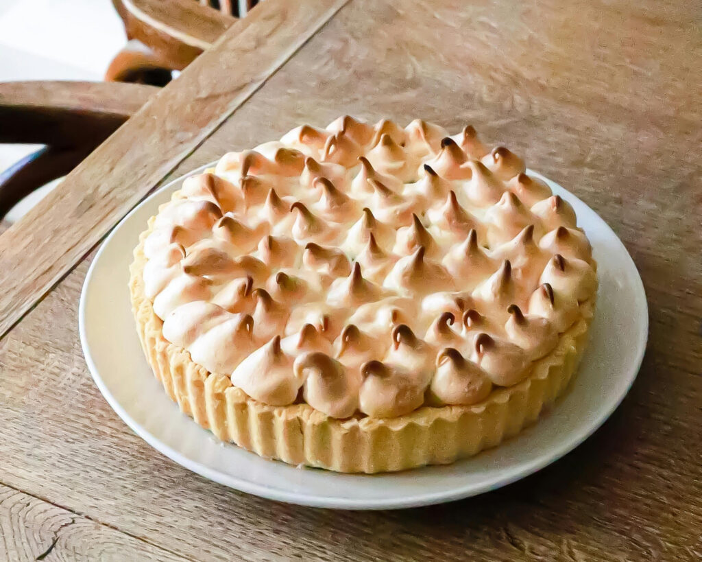 A white ceramic pale on a wooden table. On the plate is a lemon meringue pie. Photo by Geraud pfeiffer.