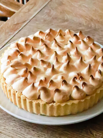 A white ceramic pale on a wooden table. On the plate is a lemon meringue pie. Photo by Geraud pfeiffer.