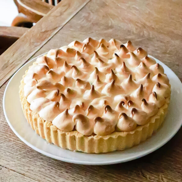 A white ceramic pale on a wooden table. On the plate is a lemon meringue pie. Photo by Geraud pfeiffer.