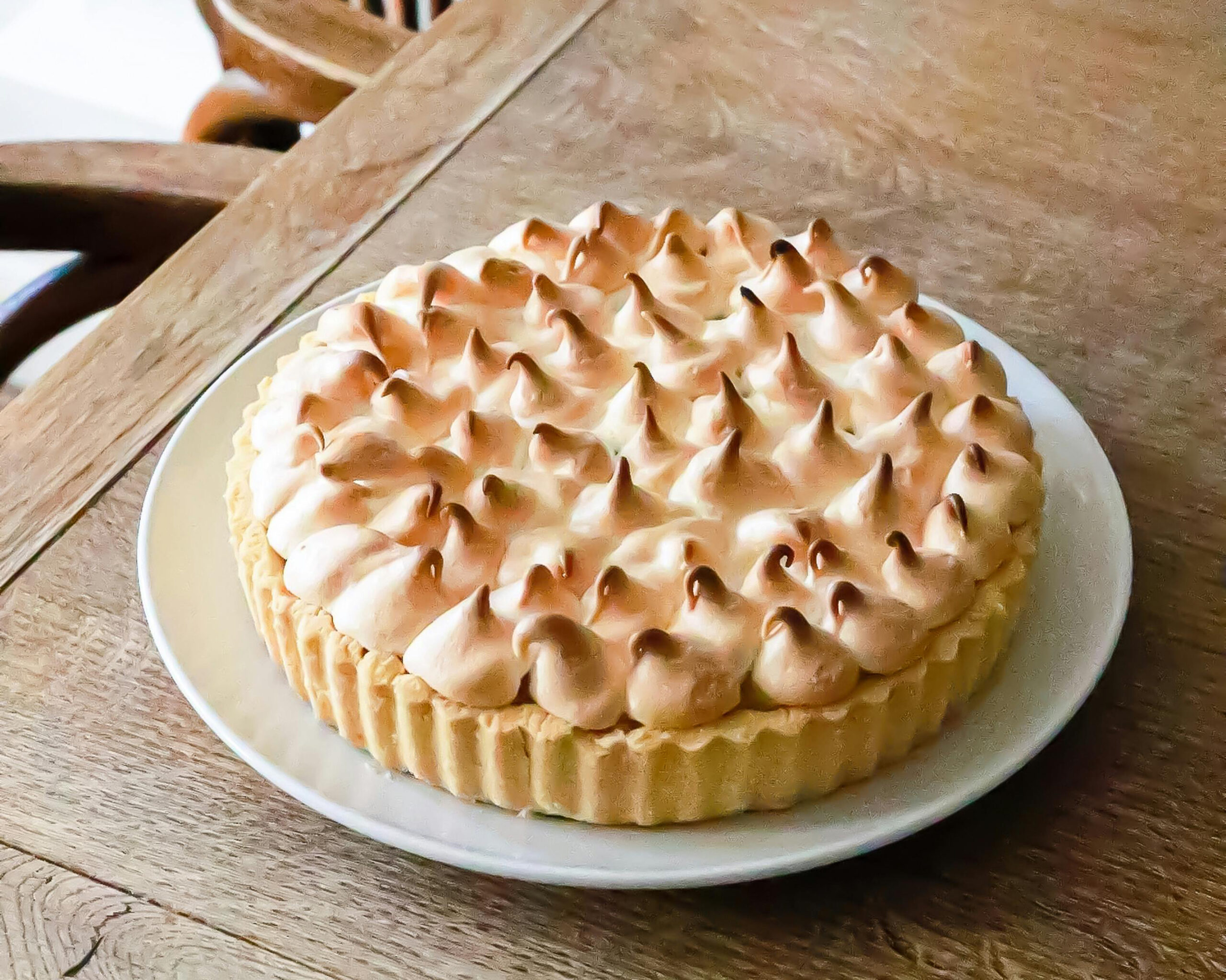 A white ceramic pale on a wooden table. On the plate is a lemon meringue pie. Photo by Geraud pfeiffer.